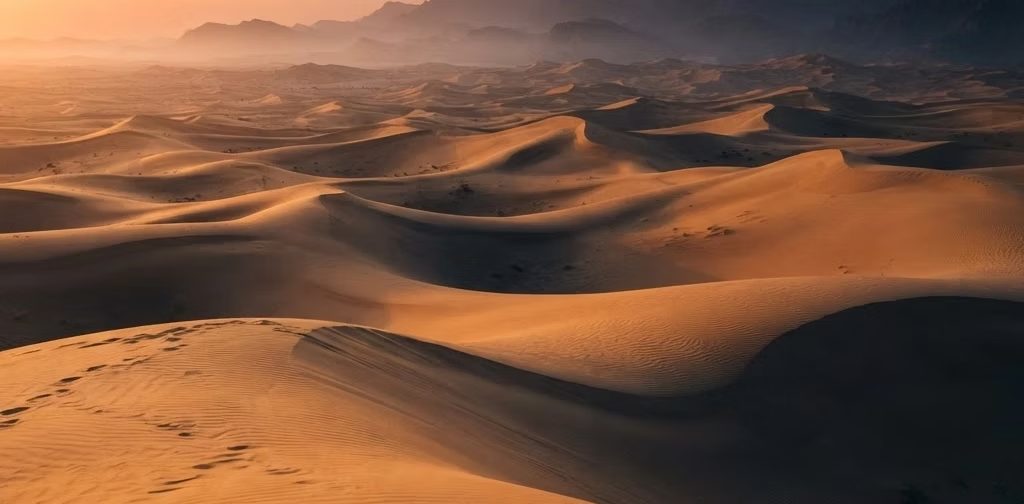 Golden sand dunes at sunrise with mountains in the distance